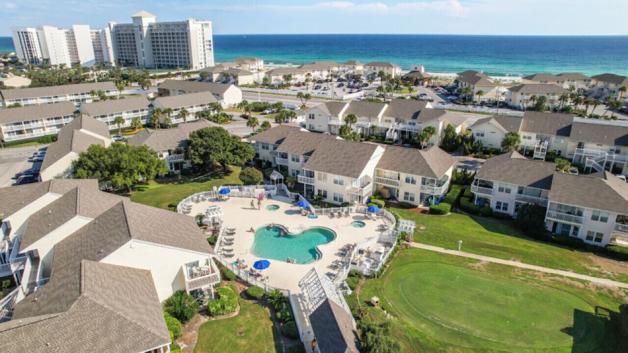 Vue aérienne d’un complexe hôtelier comprenant une piscine centrale, des villas en bord de mer et une vue sur l’océan.