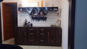 A dark wood cabinet with drawers, a coffee machine, and a shelf with bottles and glasses. - Fursat Villa (Mohali)