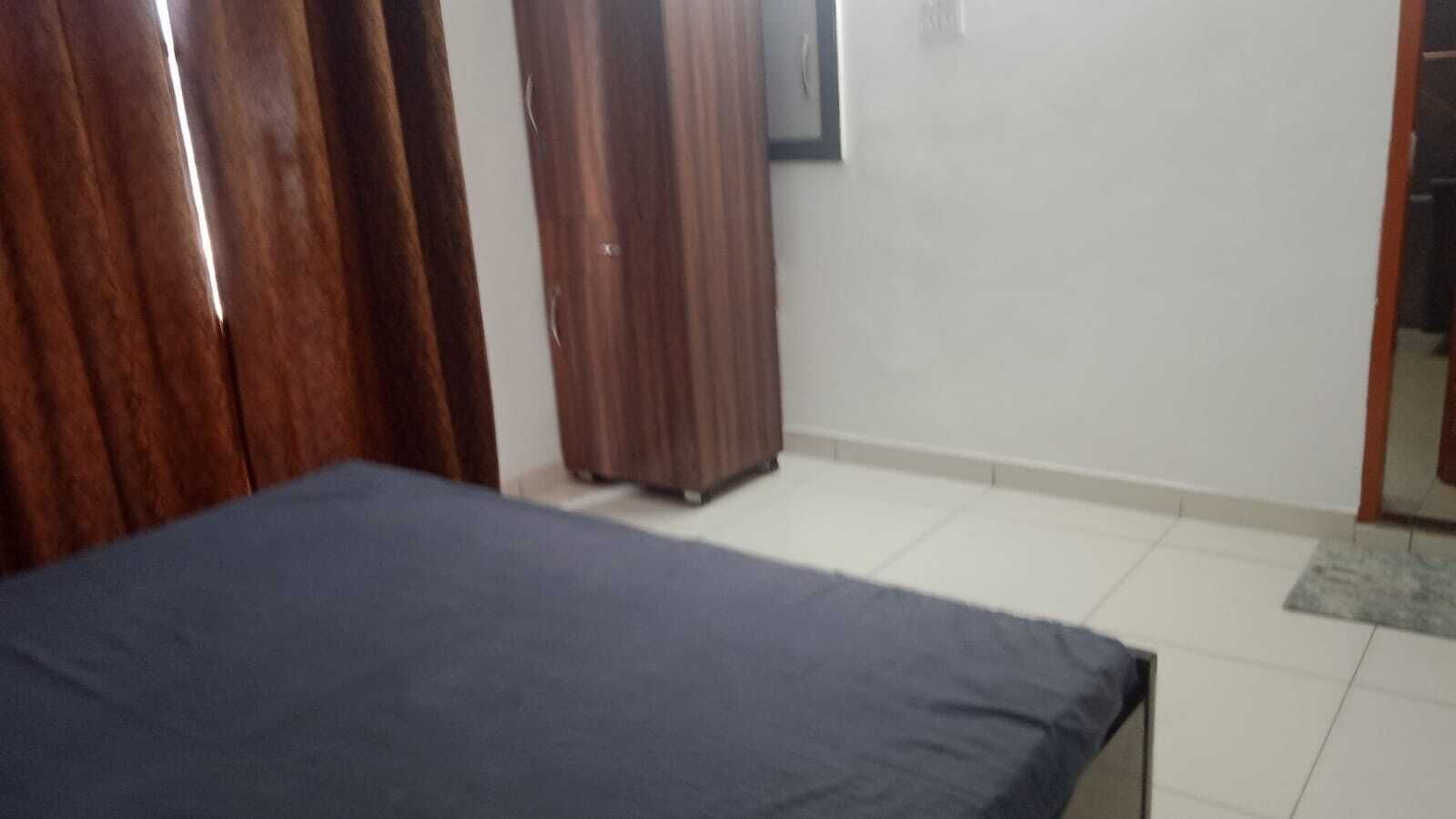 A room with a bed, wooden wardrobe, and a television on the wall.