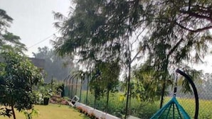 A grassy outdoor area with a swing chair, two chairs, and a garden bed. - Fursat Villa (Mohali)