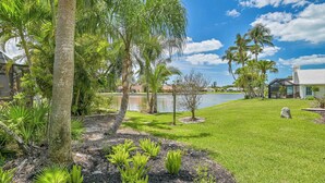 A well-maintained garden with palm trees, a lawn, and a lake.
