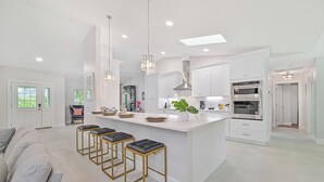 A modern kitchen with white cabinetry, a central island with stools, stainless steel appliances, and pendant lighting.