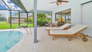 A modern indoor pool area with a glass enclosure, lounge chairs, and a ceiling fan.