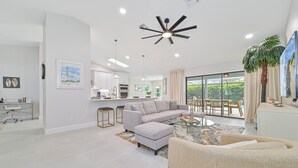 A modern living room with a gray sofa, a glass coffee table, and a dining area with a large window.