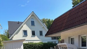 A house with a paved driveway, a white exterior, and a red roof. There is a patio area with a table and chairs. - Apartment 1 im EG mit Kitchenette (Prerow)