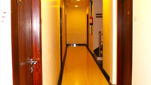 Un corridoio d'hotel con porte in legno, pavimento piastrellato e illuminazione a incasso.