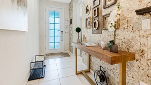 A hallway with a wooden console table, a door with frosted glass panels, and a patterned wallpaper. - Luxury Solara House W/ Pool  Near Disney (Kissimmee)