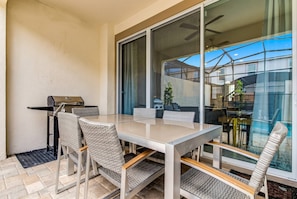 An outdoor patio with a glass door, a grill, wicker chairs, and a table.