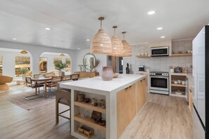 A modern kitchen with a central island, pendant lights, and a dining area with a view. - Moonstone Bungalow • Pool, Spa, Pickleball, Sauna (Joshua Tree)