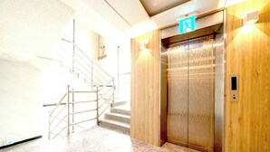 An elevator with a wooden panel design, a metal staircase with a handrail, and a wall-mounted emergency exit sign. - hotel77 (Chuncheon)