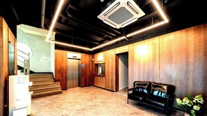 A modern lobby with a marble floor, a black leather sofa, a reception desk, and a staircase leading to an elevator. - hotel77 (Chuncheon)