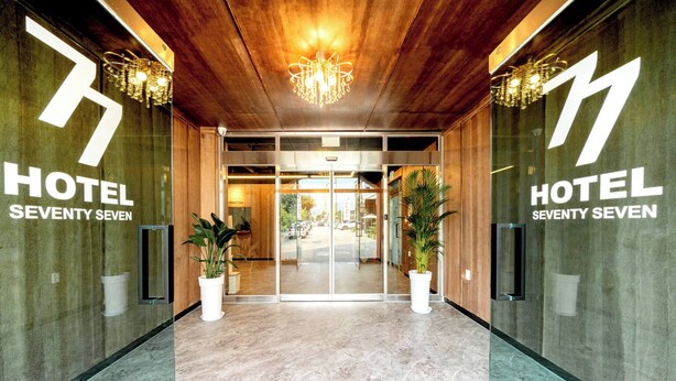 A hotel entrance with a modern design, featuring a wooden ceiling, a chandelier, and potted plants. - hotel77 (Chuncheon)