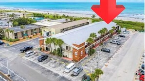 A hotel with a parking lot, a beach view, and a large building with a flat roof.