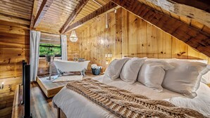 Dormitorio de cabaña de madera con una cama grande, una bañera y ventana con vistas a follaje.