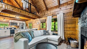Un interior de cabaña acogedor con una sala de estar que incluye un sofá seccional, una mesita redonda y una chimenea.