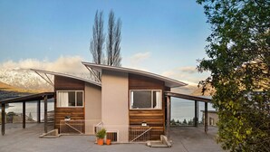 Ein modernes, zweistöckiges Haus mit Holzfassade, großen Fenstern und einer überdachten Terrasse.
