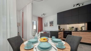 A modern dining area with a round table set for four, light blue plates and cups, and a fruit bowl.