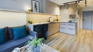 A modern kitchen with a grey sofa, a coffee table with a vase, and a dining area. - Functional Studio with Balcony | Close to Green Areas (Warszawa)