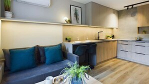 A modern kitchen with a built-in island, a dining area with a sofa, and a small side table with a plant. - Functional Studio with Balcony | Close to Green Areas (Warszawa)