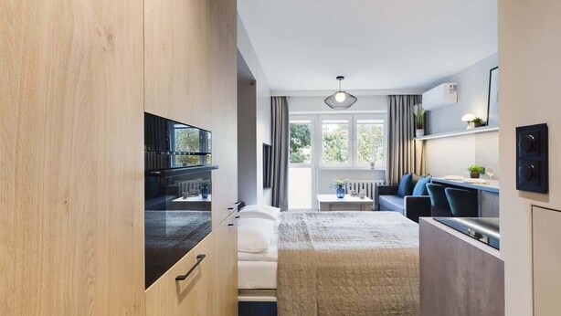 A compact hotel room with a kitchenette, a bed, a seating area, and a view of the outdoors. - Functional Studio with Balcony | Close to Green Areas (Warszawa)