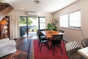 A dining area with a wooden table and chairs, a red rug, and a large window with blinds.