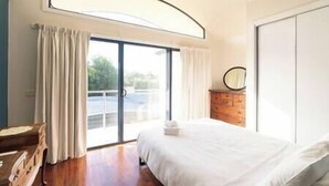 A bedroom with a large bed, a wooden dresser, a round mirror, and a sliding glass door leading to a balcony. - Clematis Hideaway (Halls Gap)