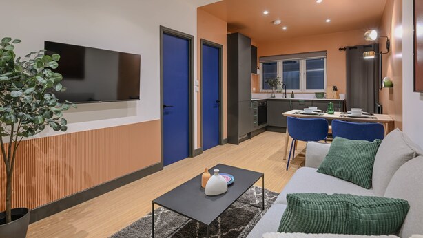 Un salon moderne doté d’un téléviseur à écran plat, d’un canapé, d’une table basse et d’un coin repas avec des chaises bleues.