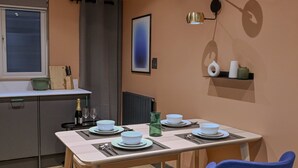 Un espace repas moderne avec une table dressée pour deux personnes, une cuisine en arrière-plan et un luminaire fixé au mur.