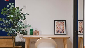 Un espace de travail comprenant un bureau, une chaise, une plante en pot et une œuvre d’art accrochée au mur.