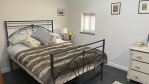 Um quarto com estrutura de cama de metal, mesa de cabeceira com abajur e cômoda.