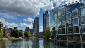 Un fiume con edifici moderni, tra cui una struttura con facciata in vetro, e un mix di architettura tradizionale e contemporanea.