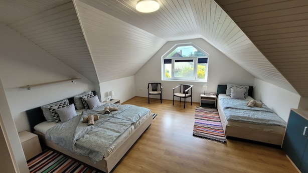 Une chambre avec un plafond en pente, une grande fenêtre, deux lits, une chaise et une petite table.