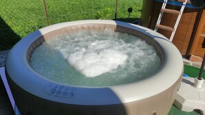 Un bain à remous doté d’un panneau de commande, entouré d’une zone herbeuse et d’une clôture en bois.