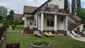 Une maison à deux étages dotée d’un balcon, d’un espace de jeux et de coins salon extérieurs.