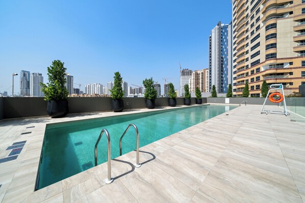 A rooftop pool with clear blue water, surrounded by potted plants and a city skyline in the background. - Waves - Cityscape Balcony Views and Cozy Comfort in Dubai (Dubai)
