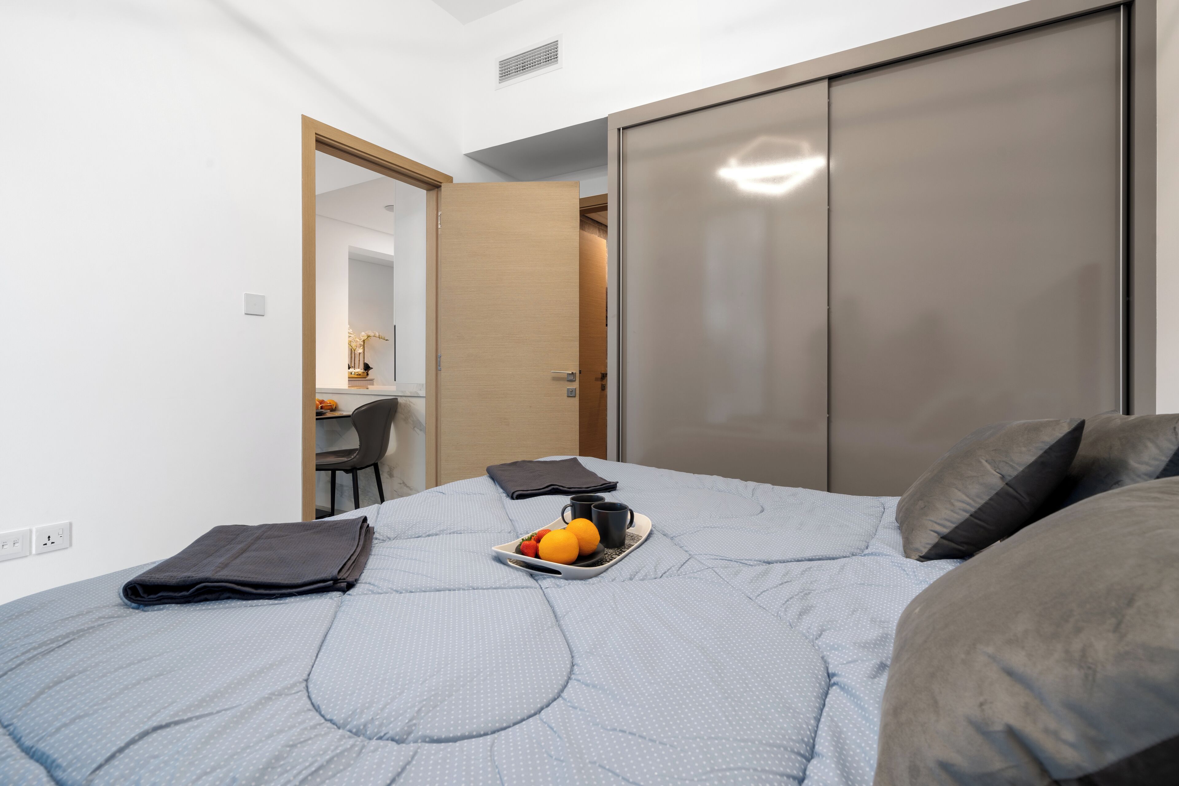 Un dormitorio con cama, una bandeja con fruta y una taza, un escritorio con silla y un armario.