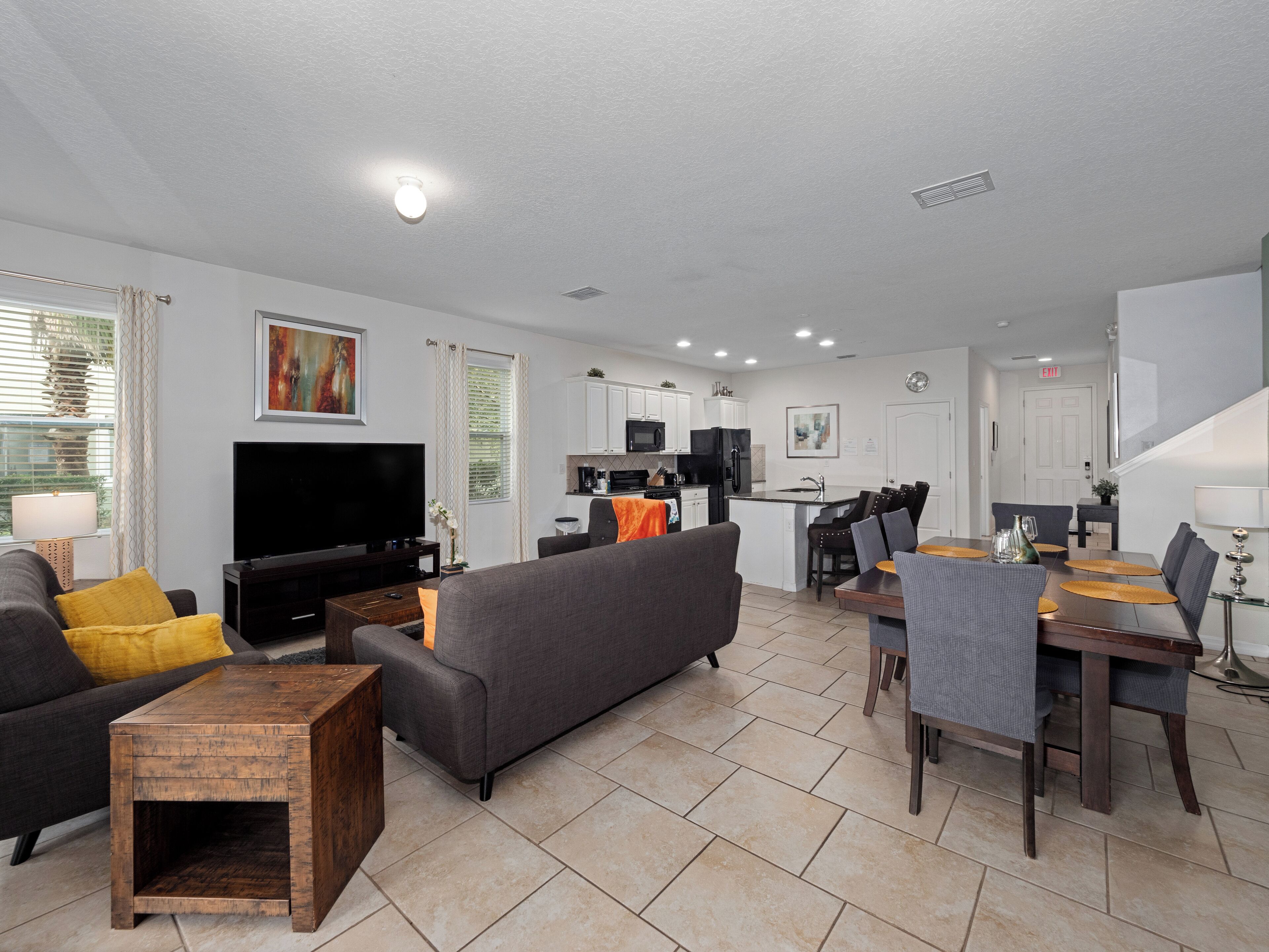 A modern living room with a flat-screen TV, grey sofa, wooden coffee table, and a dining area with a wooden table and chairs.