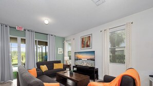 Un salon moderne avec un canapé, une table basse et un téléviseur. Il y a un tableau au mur et une fenêtre avec des rideaux.