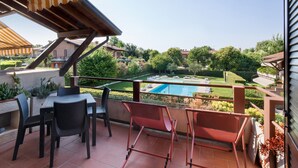 Un balcon avec une table et des chaises, donnant sur une piscine et un jardin.