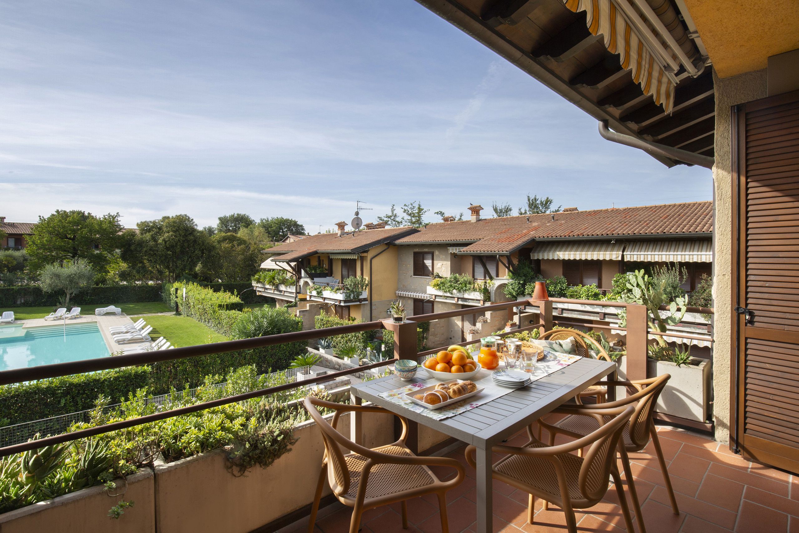 Un balcón con mesa dispuesta para el desayuno, con vista a una piscina y un jardín.