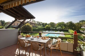 Une terrasse avec une table préparée pour le petit-déjeuner, donnant sur une piscine et une végétation luxuriante.