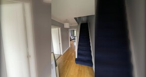 A hallway with a staircase leading to a dark room, wooden flooring, and a door at the end. - Large 3BD Duplex, 20Min to Airport (Dublin)