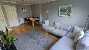 A living room with a grey sofa, a glass coffee table, a dining table with chairs, and a painting on the wall. - Large 3BD Duplex, 20Min to Airport (Dublin)