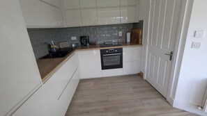 Eine kleine Küche mit weißen Schränken, einem eingebauten Backofen und einer grauen gefliesten Spritzschutzwand.