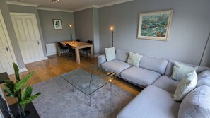 A living room with a grey sofa, a glass coffee table, a dining table with chairs, and a painting on the wall. - Large 3BD Duplex, 20Min to Airport (Dublin)