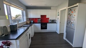 A modern kitchen with white cabinets, a black countertop, a red backsplash, a stainless steel refrigerator, and a washing machine. - Bright 2BD Family Home with Hidden Zen Den & Garden (Dublin)