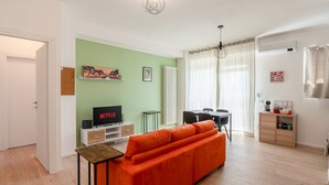 Ein Wohnzimmer mit einer Couch, einem Fernseher, einem Esstisch und einem Schrank.