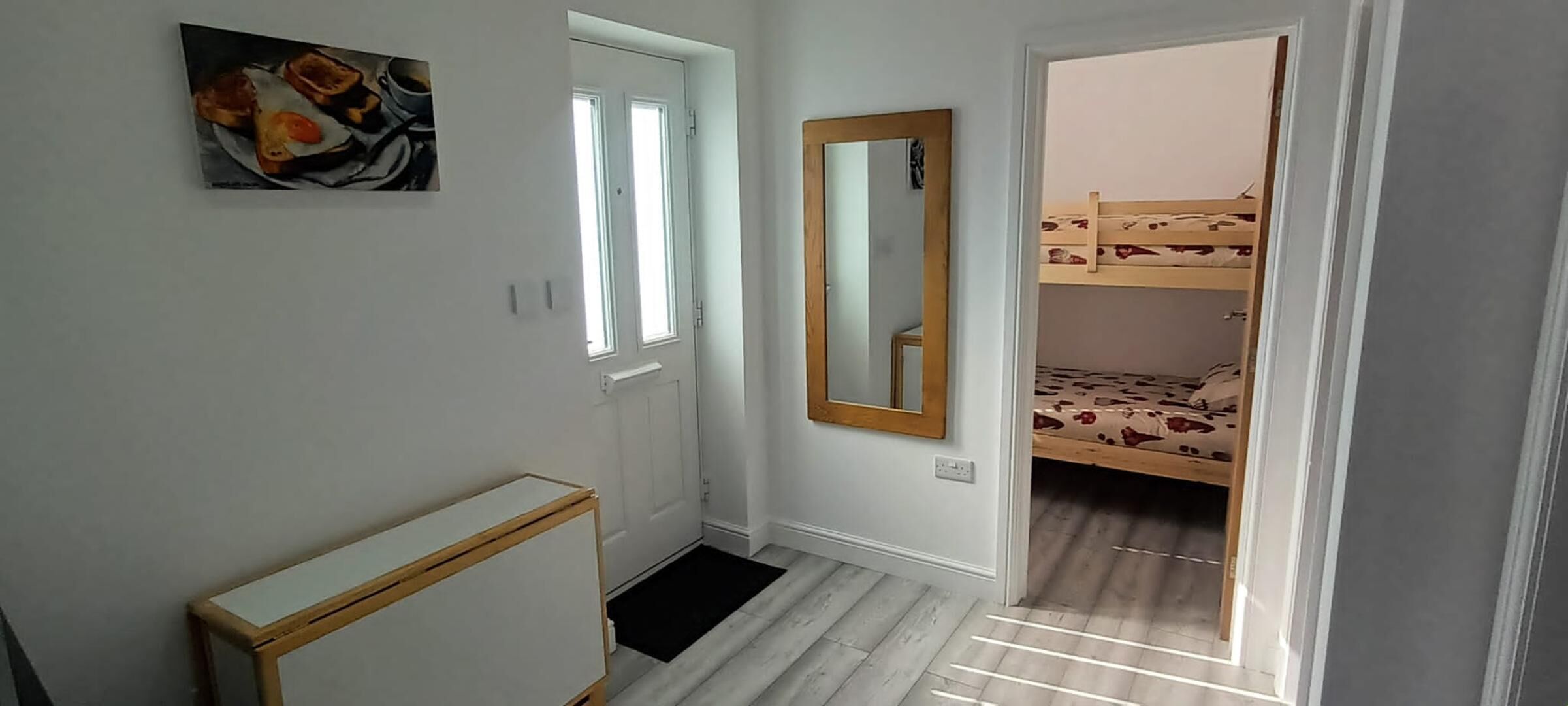 Een slaapkamer met een stapelbed, een nachtkastje, een spiegel en een deur naar een andere kamer.