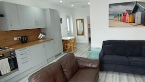 Una cucina moderna con mobili grigi, un piano di lavoro in legno e un'area pranzo con tavolo e sedie. C'è un divano nero e una lampada nella zona living.