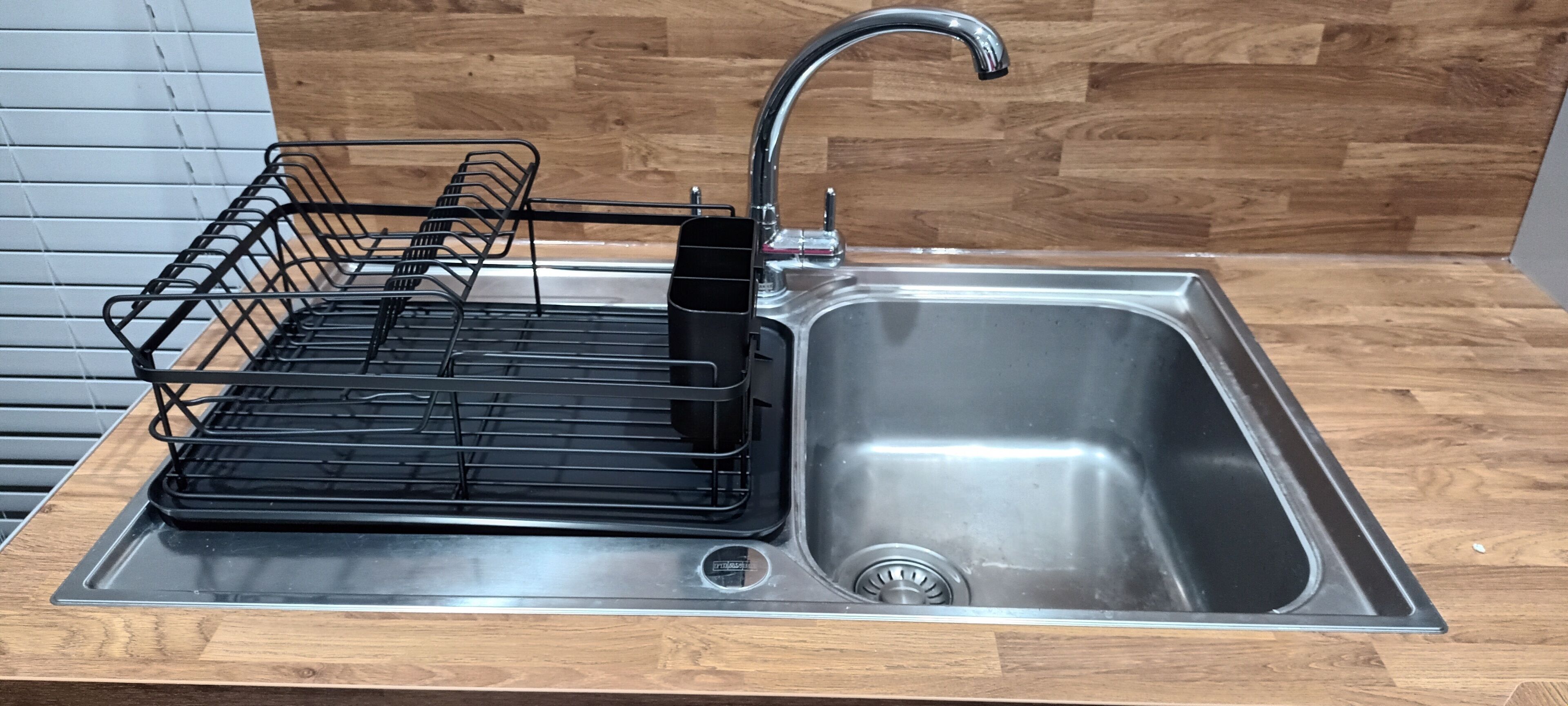 Un lavamanos de acero inoxidable con un escurreplatos negro y un grifo moderno.